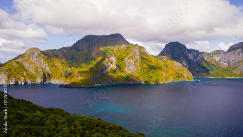 Tableau sur toile A scenic view of a lush green mountainous coastline, bathed in sunlight, capturing the essence of nature’s majesty and the allure of remote, natural landscapes
