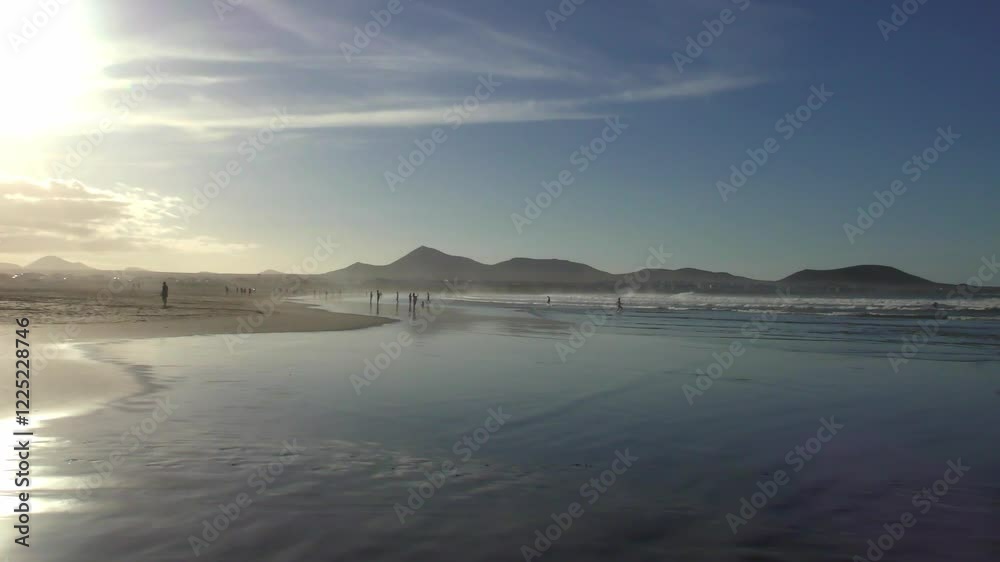Sandstrand mit Menschen in der Abendsonne bei stimmungsvollem Sonnenuntergang, Meer, Caleta de Famarar, Urlaub, Idylle, Lanzarote, Kanaren, Küste, Landschaft, Bergsilhouetten, Surfer
