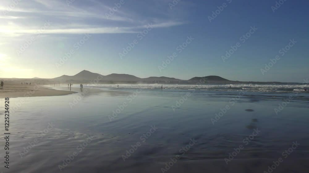 Sandstrand mit Menschen in der Abendsonne bei stimmungsvollem Sonnenuntergang, Meer, Caleta de Famarar, Urlaub, Idylle, Lanzarote, Kanaren, Küste, Landschaft, Bergsilhouetten, Surfer
