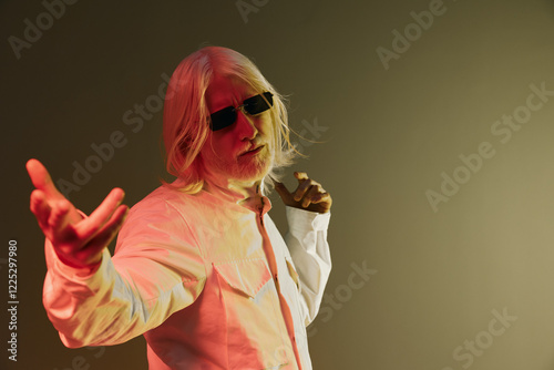 Stylish older man with white hair and sunglasses in a modern white shirt striking a pose against a gradient colored background, showcasing confidence and charisma photo