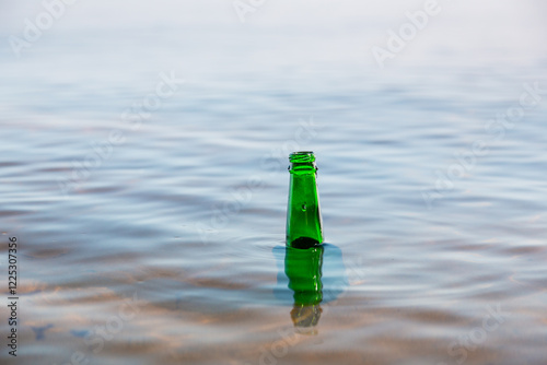 Green glass bottle floating in a river, bottleneck seen over water surface.