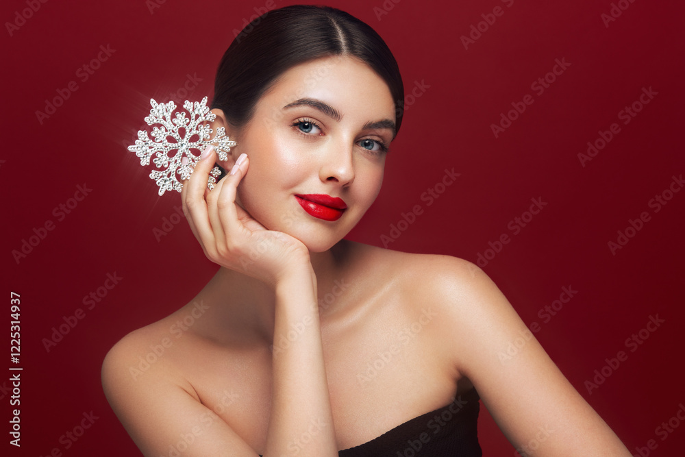 Beautiful young woman with red lipstick, shiny clean skin and face, showing glowing snowflake, near face and smiling, isolated on a red background. Christmas holidays concept Beautiful young woman with red lipstick, shiny clean skin and face, showing glowing snowflake, near face and smiling, isolated on a red background. Christmas holidays concept