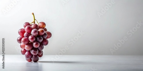 A single bunch of red grapes rests on a minimalist white surface against a bright background