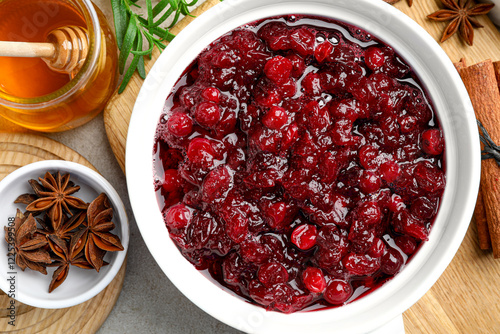 Tasty cranberry sauce in gravy boat, honey and spices on grey table, top view photo