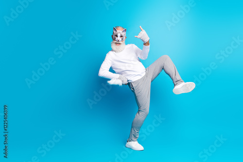 Elderly man cosplaying as a feline-themed character strikes a playful pose against a vivid blue studio background photo