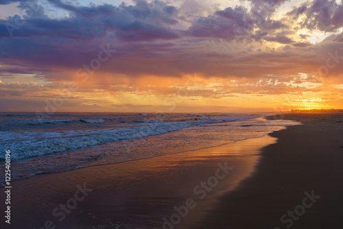 Rich orange and purple hues illuminate the shoreline as the sun sets.