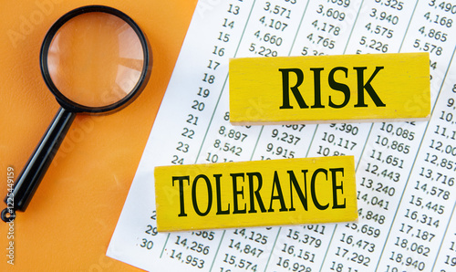 RISK TOLERANCE - words on yellow wooden blocks on the background of a magnifying glass and a table with numbers