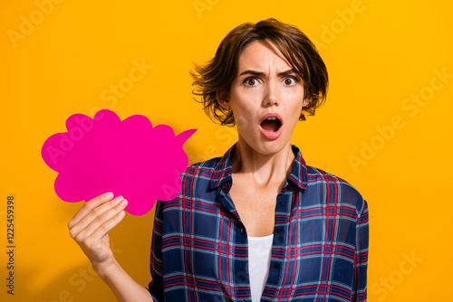 Portrait of offended gloomy girl with bob hairstyle wear checkered shirt hold dialog bubble open mouth isolated on yellow color background