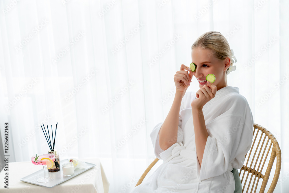 Woman holding slices of fresh cucumber and wearing bathrobe enjoying luxurious facial skincare spa in resort or hotel. Skin treatment for face and beauty care. Quiescent Woman holding slices of fresh cucumber and wearing bathrobe enjoying luxurious facial skincare spa in resort or hotel. Skin treatment for face and beauty care. Quiescent