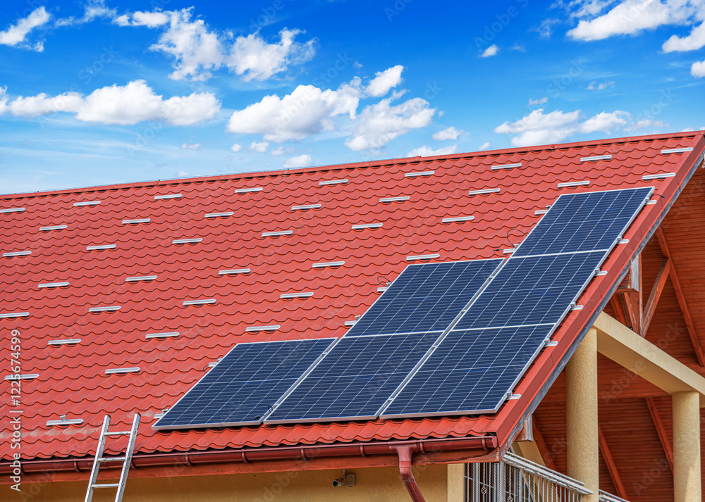 A set of solar panels is installed on the roof of a building with red tiles under a clear blue sky.