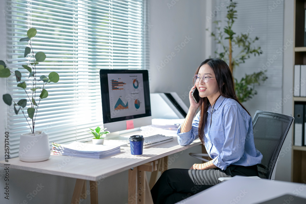 A woman is sitting at a desk with a computer monitor and a cell phone A woman is sitting at a desk with a computer monitor and a cell phone