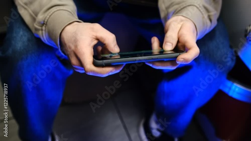 Young man playing mobile game with fast finger movements and colorful pulsating hand lights, dynamic gameplay, close up phone screen, digital entertainment, gaming action, energetic gaming session.