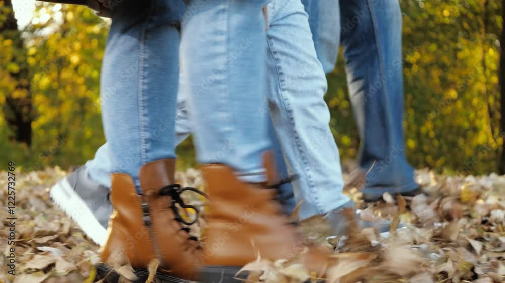 Legs of family stroll along park path. Steps of legs of family on leaves carpet during walk in park. Legs of family mother father and child walking on path covered with yellow leaves in park Legs of family stroll along park path. Steps of legs of family on leaves carpet during walk in park. Legs of family mother father and child walking on path covered with yellow leaves in park