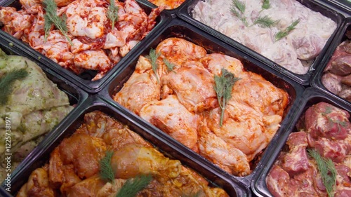 Smooth camera movement, assortment of raw meat preparations in a store window. On the counter are kebabs, marinated meat, chicken parts, pieces of beef, sliced pork with seasonings, spices, marinades.
