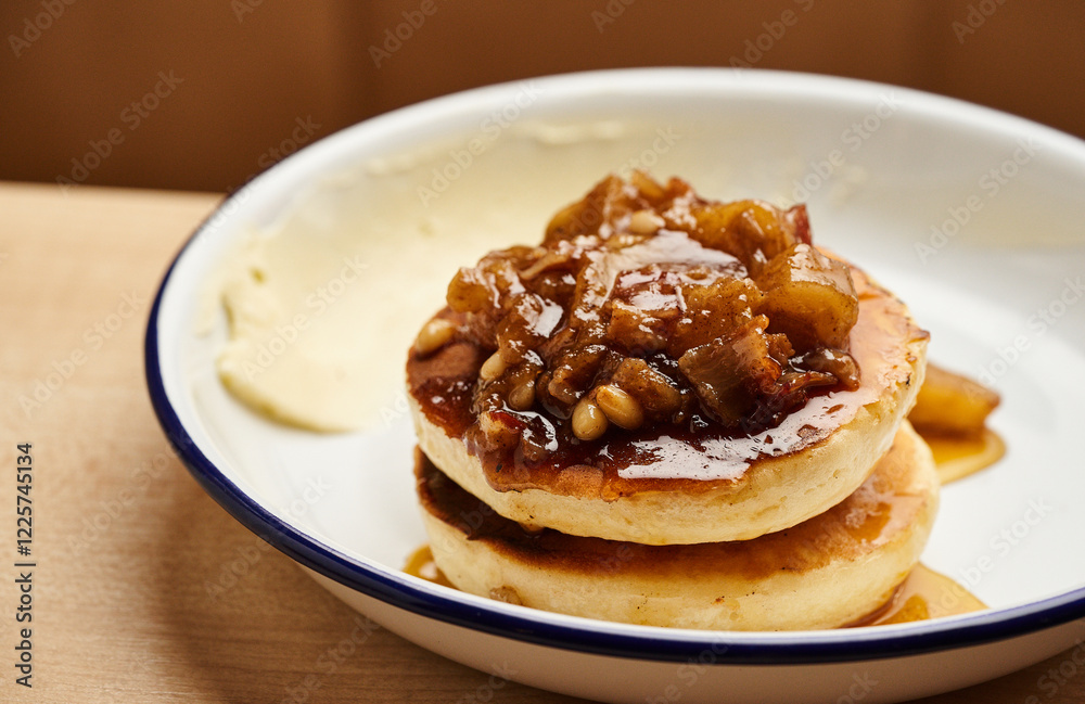 Two fluffy pancakes stacked and drizzled with caramelized apple topping and nuts are served in a cozy cafe setting during breakfast Two fluffy pancakes stacked and drizzled with caramelized apple topping and nuts are served in a cozy cafe setting during breakfast
