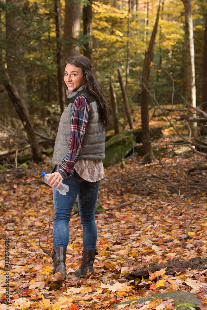 Cute young brunette woman poses for photo in forest hiking with bottle of water Cute young brunette woman poses for photo in forest hiking with bottle of water