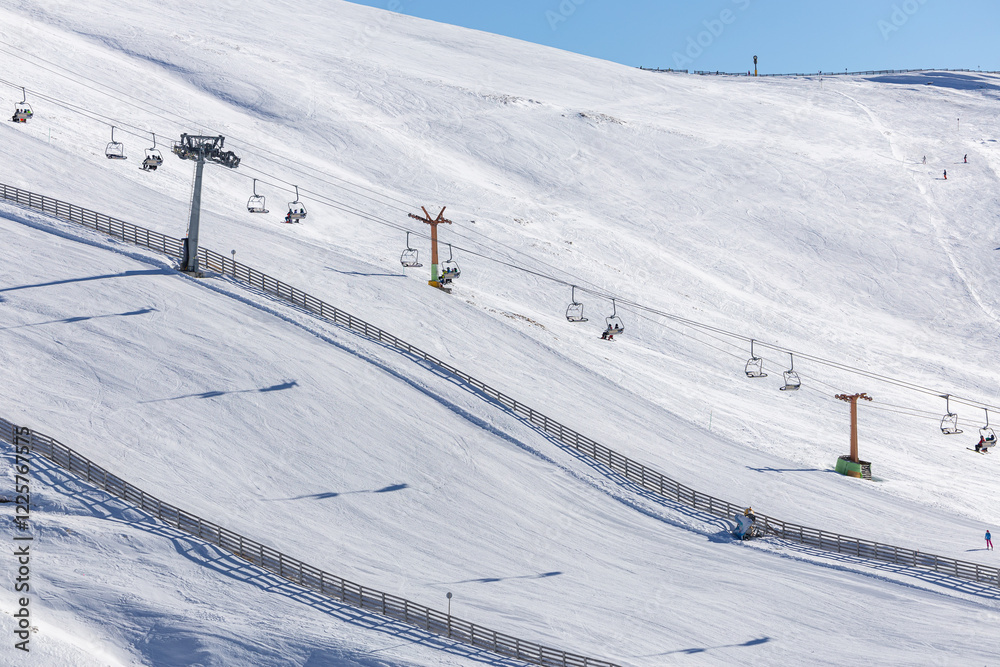 Skiers and snowboarders enjoy the breathtaking view from chairlifts at Cota 2000, Sinaia, Romania, with mountain peaks in the distance under a serene winter sky. Ski in the Romanian mountains.