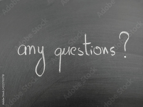 Handwritten phrase any questions written in white chalk on a blackboard background