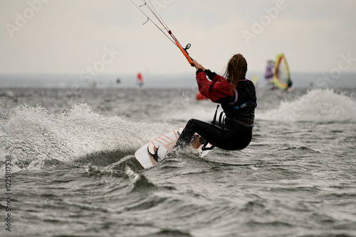 Female kiteboarder holds on to the handle of the kite on her surfboard photo