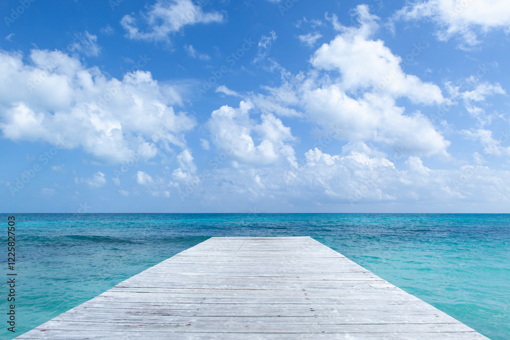 Fototapeta premium Ocean Pier with Cloudy Sky in the Background, a wooden pier extends into a serene turquoise ocean under a vibrant blue sky dotted with fluffy white clouds.