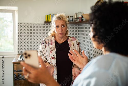 Lesbian couple arguing over smartphone in kitchen photo