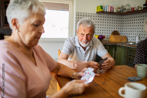 Senior friends playing cards together at kitchen table photo