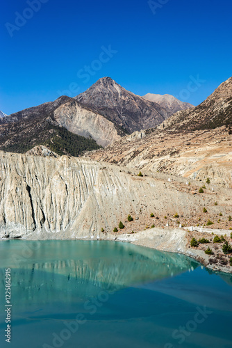 Turquoise ice covered Gangapurna Tal lake and the rocky mountains behind it. Chongkor viewpoint near Manang village, a side trip for acclimatisation on Annapurna circuit trekking, Nepal. photo