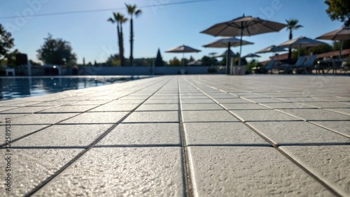 A medium closeup shot of a newlyinstalled antislip pool deck surface showcasing textured tiles under a sunlit sky with shadows cast from surrounding umbrellas. photo