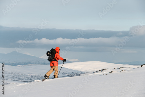 Close-up of a skier in an orange jacket and full gear skiing across the snow