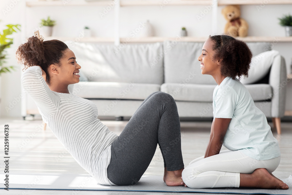 Joyful black mother and kid in sportswear training together at home, sitting on fitness mat, working on abs, doing crunches, side view. Sporty family mom and daughter doing work out Joyful black mother and kid in sportswear training together at home, sitting on fitness mat, working on abs, doing crunches, side view. Sporty family mom and daughter doing work out