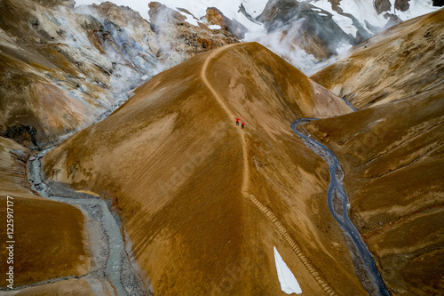 Scenic aerial drone view of a couple hikers in red jackets and foggy Kerlingarfjoll mountain path amidst desert and snowy terrain in Iceland