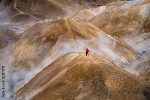 Scenic aerial drone view of a man hiker in red jacket and foggy Kerlingarfjoll mountain path amidst desert and snowy terrain in Iceland
