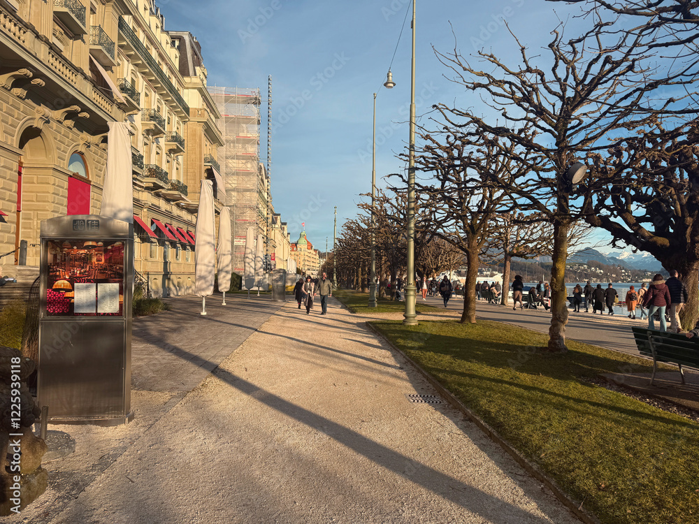 Obraz premium Sunny Promenade in Lucerne. High quality photo The beautiful lakeside promenade in Lucerne shines under the warm sun, offering a perfect place for a leisurely stroll. The clear blue sky, shimmering