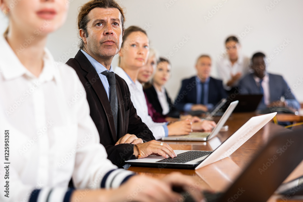 Businessman using laptop during conference in meeting room. Man sitting at desk with colleaugues. Businessman using laptop during conference in meeting room. Man sitting at desk with colleaugues.