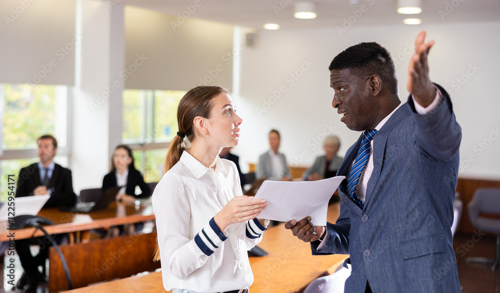Obraz premium Irate adamant middle aged african male director dismissing frustrated and upset young white female subordinate employee for incompetence telling her to get out of office pointing to the door at