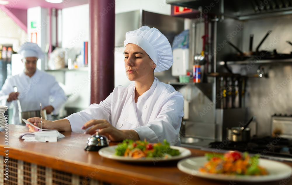 Female cook reads the paid check and presses the bell for the waiter in the restaurant Female cook reads the paid check and presses the bell for the waiter in the restaurant