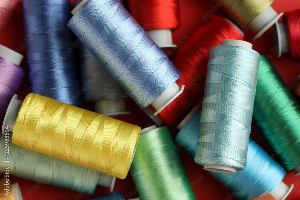 Different spools of sewing threads on red background, top view Different spools of sewing threads on red background, top view
