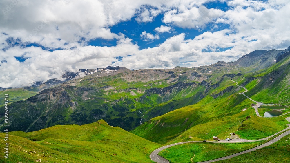 Obraz premium The Grossglockner High Alpine Road in Kaprun, Austria, offers breathtaking views of the Alps. This scenic drive winds through green valleys and past towering mountains.