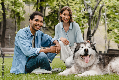 Happy cheerful dog owners walking with fluffy pet outdoors. Young woman and man couple friends boyfriend and girlfriend playing taking care of malamut in city park together photo