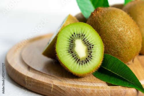 Ripe kiwi fruits in sunlight. Heap of whole kiwi fruits with green leaves and fresh cut kiwi on wooden cutting board. Healthy organic fruits full of vitamins and antioxidants.