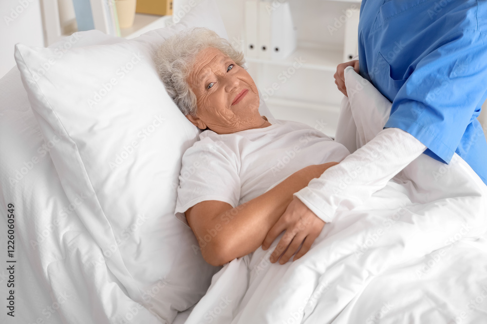 Obraz premium Female nurse putting senior woman to bed in bedroom