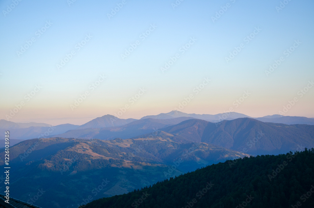 Tranquil landscape capturing layers of mountains in soft evening light, creating peaceful and serene scenery with gradients of color transitioning into the clear twilight sky. Carpathians, Ukraine