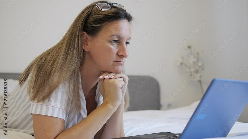 Woman focused on typing content on laptop while lying on bed near window Typing scene highlights concentration and precision Typing process emphasizes relaxed yet productive workflow in cozy bedroom Woman focused on typing content on laptop while lying on bed near window Typing scene highlights concentration and precision Typing process emphasizes relaxed yet productive workflow in cozy bedroom