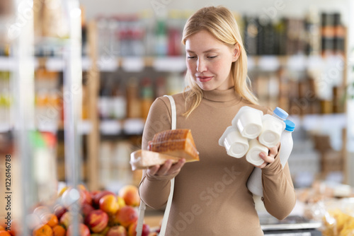 Girl with dairy products chooses something else, examines labels of cheese and yogurt, interested in composition and expiration date. Client examines packaging, looking for something for breakfast photo