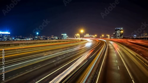 Vibrant city skyline at night with illuminated buildings, showcasing light trails from vehicles on highway, creating dynamic urban atmosphere and lively traffic illumination.