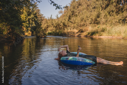Woman laying on inflatable donut floating in creek fully dressed