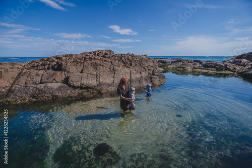 Mum holding baby exploring rock pool