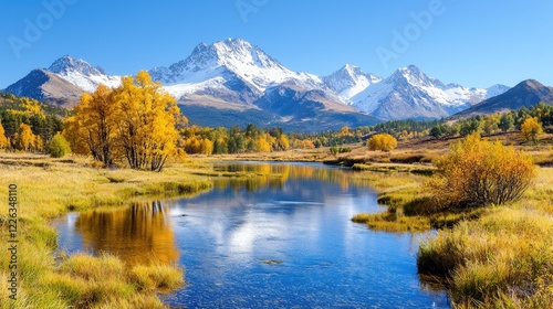 Snow-capped mountain peaks rise behind a winding river lined with golden autumn trees under a clear blue sky.