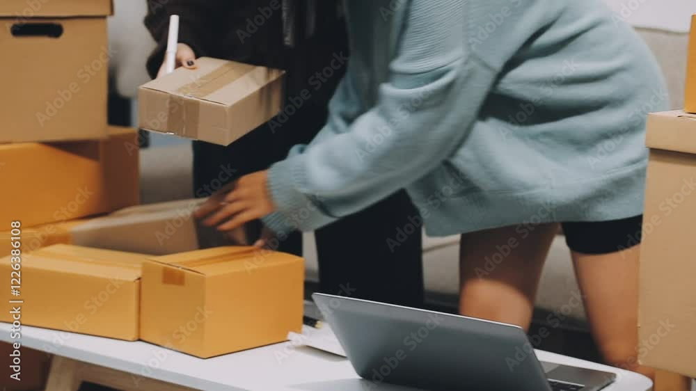 Startup SME small business entrepreneur of freelance Asian woman wearing apron using laptop and box to receive and review orders online to prepare to pack sell to customers, online sme business ideas.