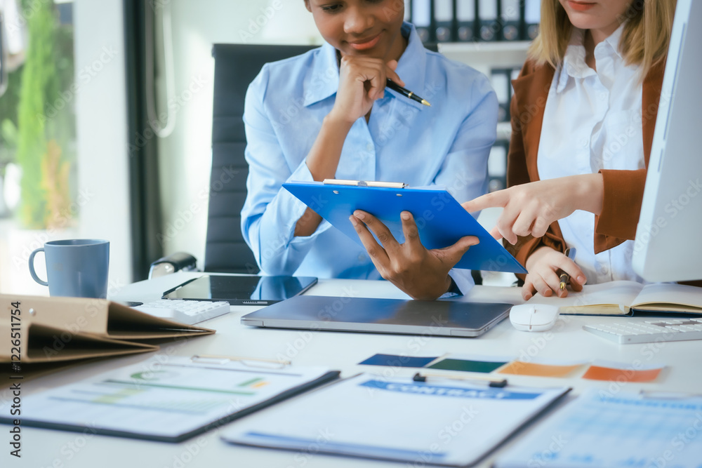 Fototapeta premium An African American businesswoman and a Caucasian woman work at analyzing market data, developing business strategies,discussing financial growth while using a laptop spreading money for investment